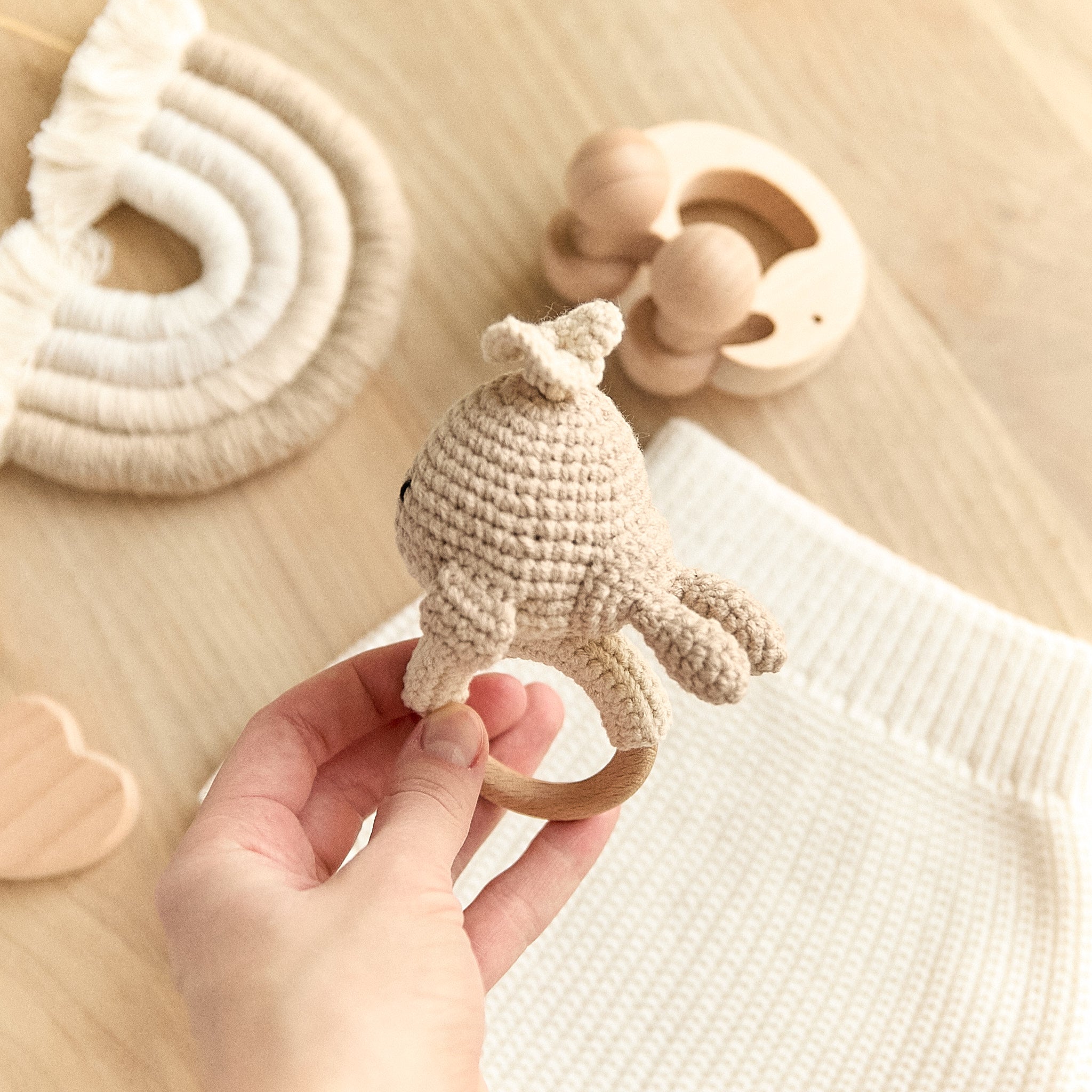Handmade crochet whale baby rattle held in hand — natural wooden ring size reference
